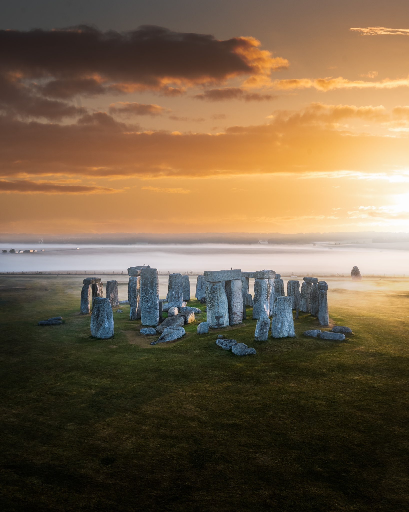 An aerial shot of Stonehenge at sunrise with mist on the horizon.